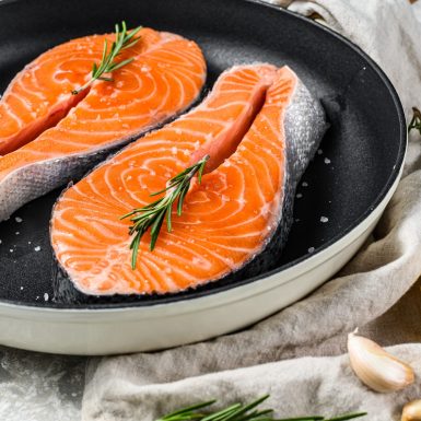 Raw salmon steak in a frying pan. Healthy seafood. Gray background. Top view.