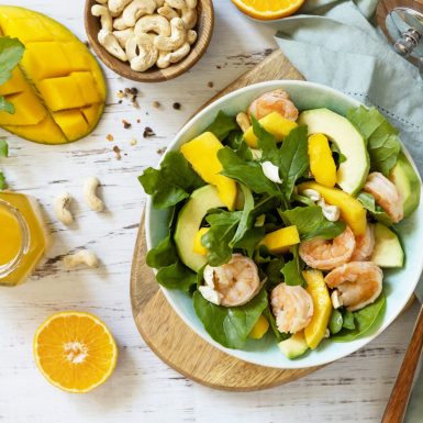 Vegetarian vegan healthy food. Salad with arugula, mango, avocado, shrimp, pecans and dressing of olive oil, honey and wine vinegar on a white rustic kitchen table. Top view, flat lay background.